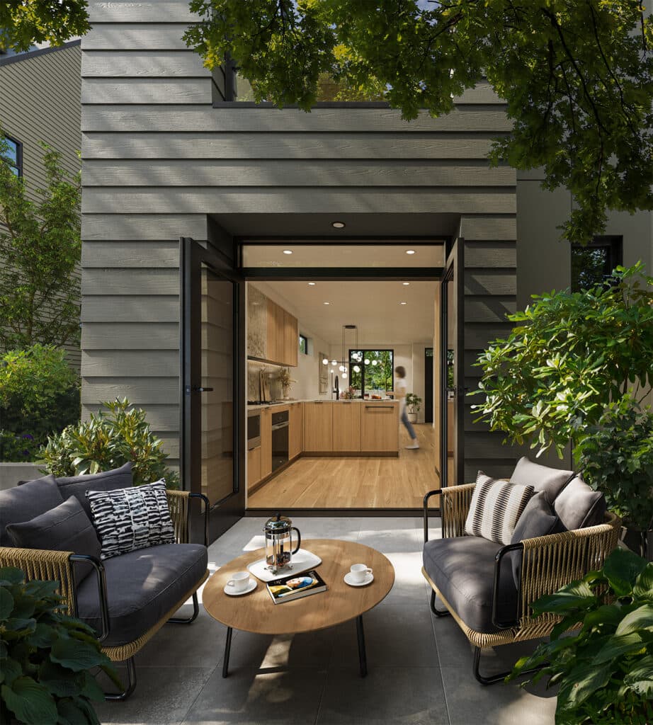 Whitford – A ground-level view of a private patio featuring dark woven armchairs and a wooden coffee table set with coffee cups. Open glass doors lead directly into a modern, light-filled kitchen with warm wood cabinetry and light hardwood flooring.