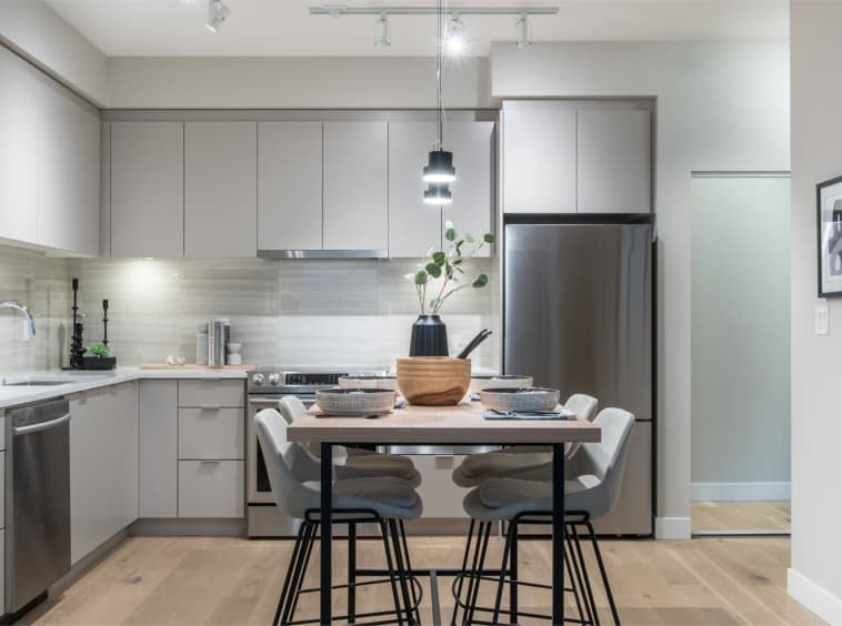 Crescent Court – Compact condo kitchen with light grey cabinets, stainless steel appliances, and a small dining table with grey upholstered chairs.