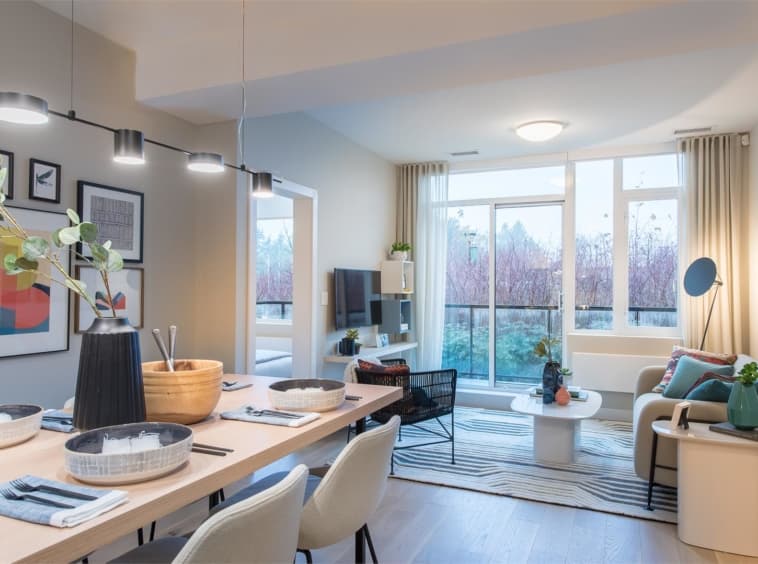 Crescent Court – Open living and dining area with a wood dining table, gallery wall of framed art, and a grey sofa facing a balcony with sliding glass doors.