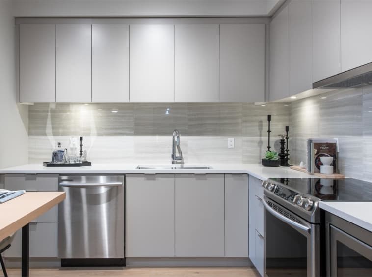 Crescent Court – Kitchen close-up showing light grey cabinetry, a tiled backsplash, stainless dishwasher, and gas range with black candlesticks on the counter.