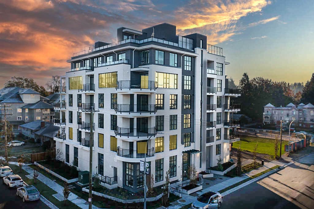 One Shaughnessy – Aerial view at dusk of a white and dark mid-rise condo building on a corner lot, lit up from within, surrounded by houses, trees, and streets.
