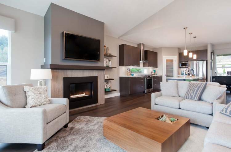 Camden at The Falls – Open-concept living room with a fireplace, wall-mounted TV, and adjoining dark-cabinet kitchen.