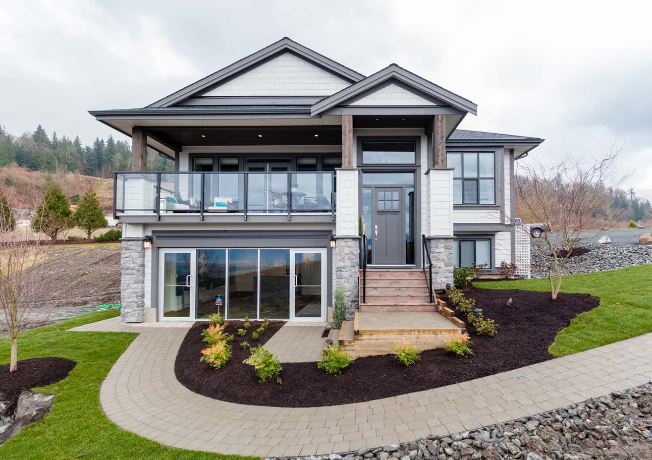 Camden at The Falls – Front exterior of a two-story home with grey shingle siding, stone accents, a covered entry porch, and landscaped beds.