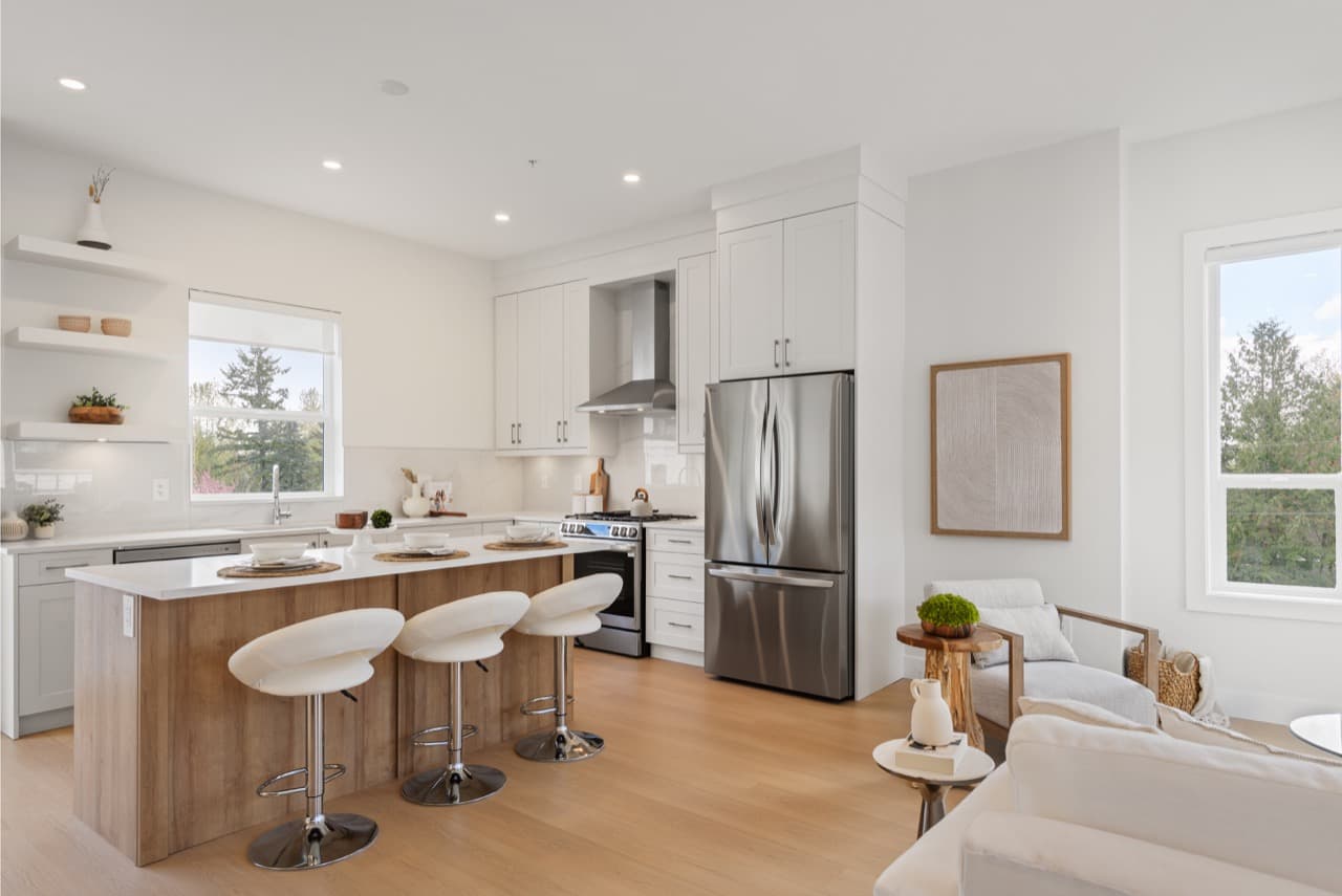 Gordon Square – Open kitchen and living area with white cabinetry, a wood island with white stools, stainless appliances, and a cozy seating nook by a window.