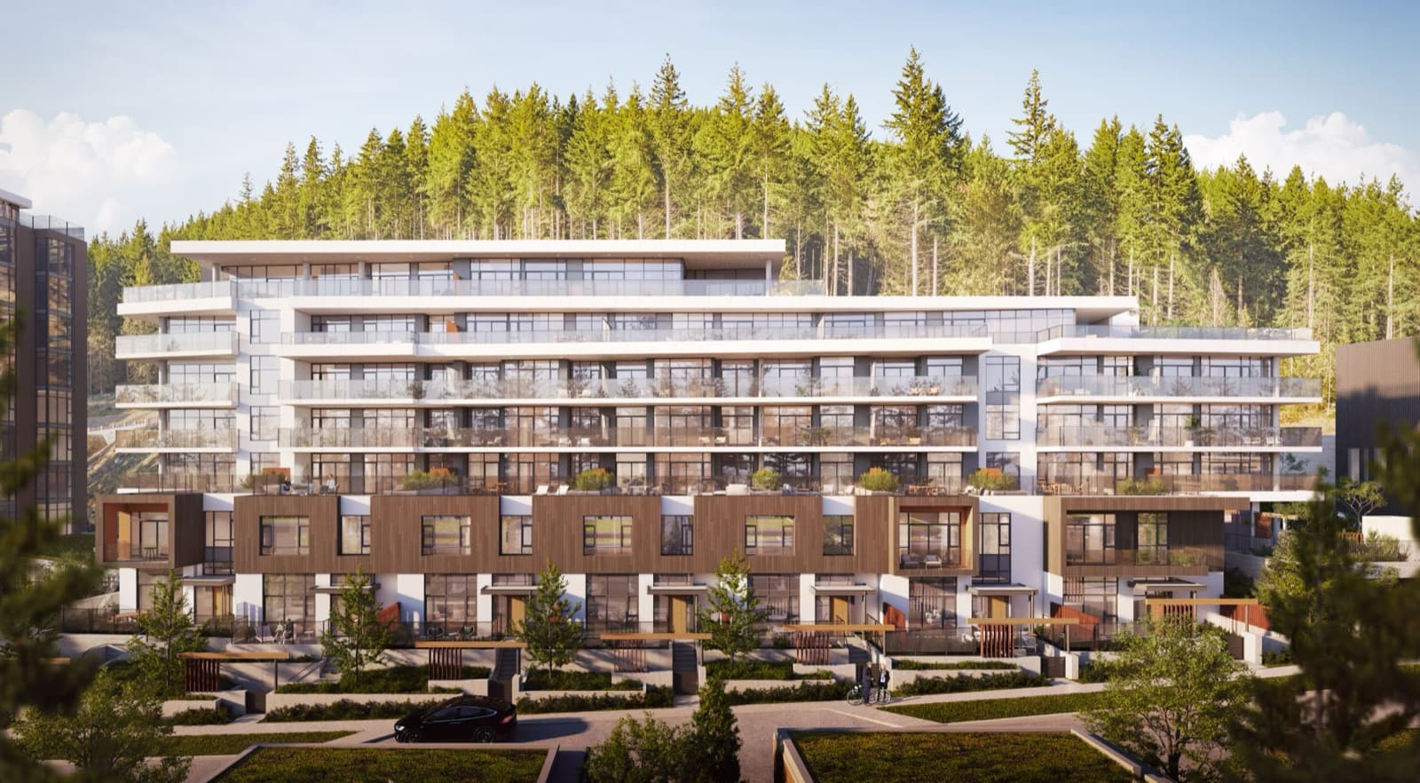 Hawksley – Street-level view of the multi-storey residential building with wood-toned townhome units in front, backed by a forested hill.