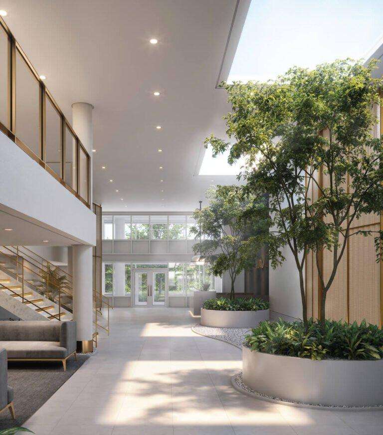 Juno Condos – Double-height lobby atrium with a skylight, mature indoor trees in round planters, a brass-screened mezzanine and lounge seating.
