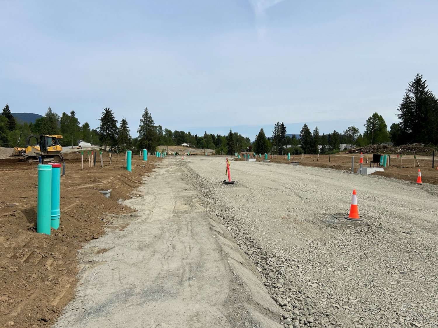Tunbridge Crossing – Graded gravel roadway through the development lot lined with utility riser pipes, a bulldozer working at left, cones marking the path.