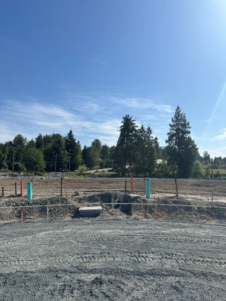 Tunbridge Crossing – Cleared construction lot with survey stakes and utility markers, a road and trees visible in the background.