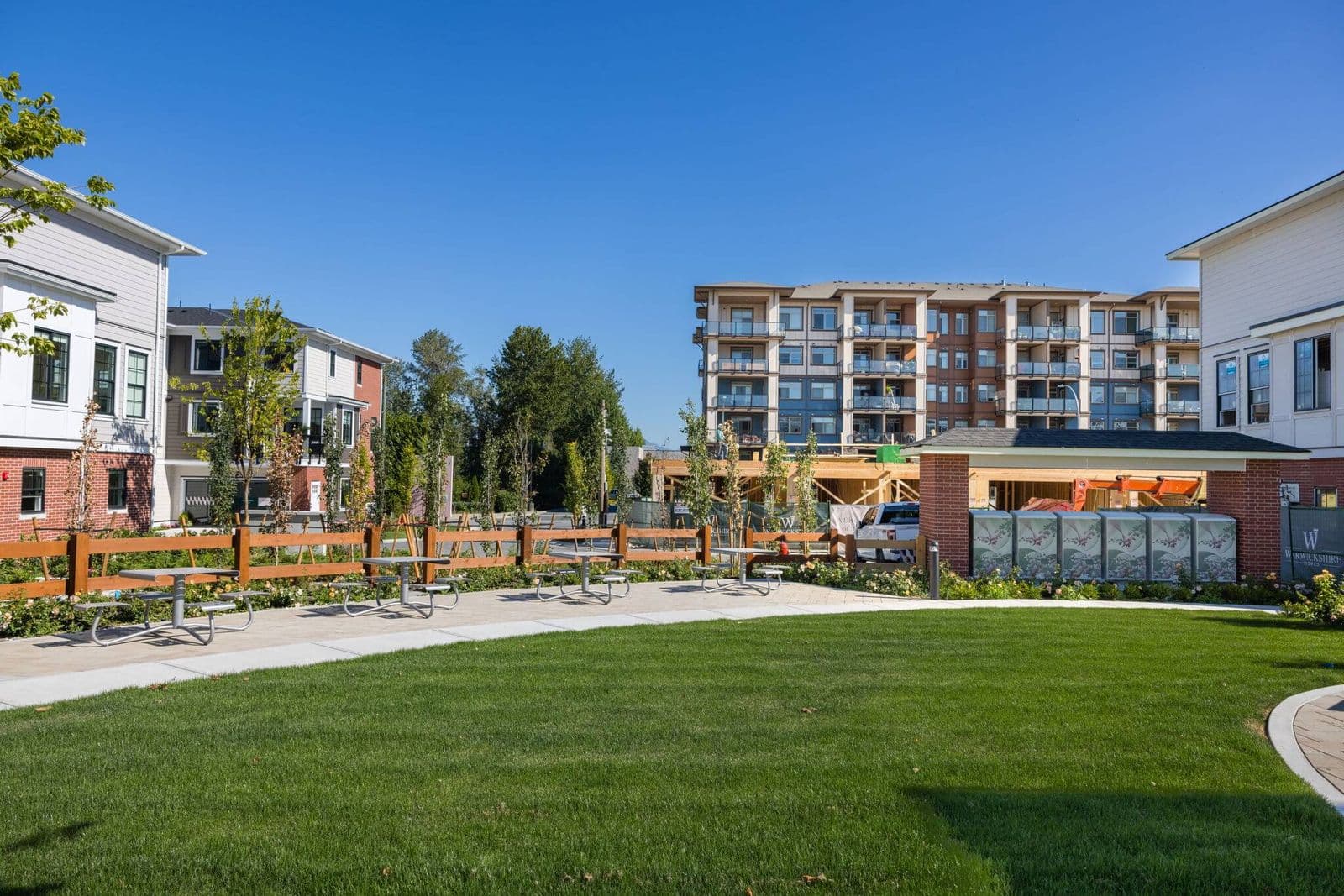 Townside Village – Ground-level photo of the shared amenity lawn and picnic area with a condo building and townhomes under construction behind.