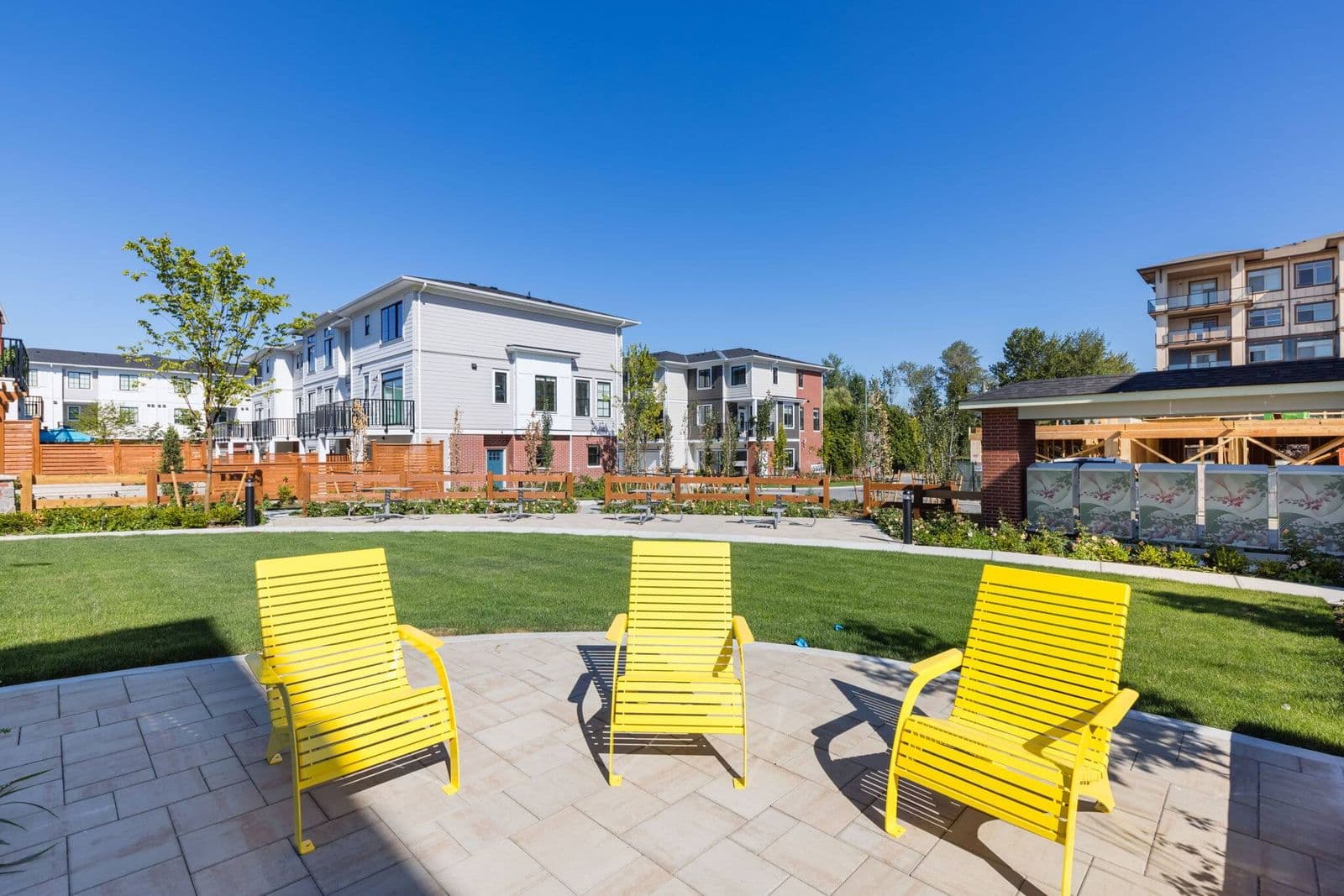 Townside Village – Photo of bright yellow lounge chairs on the shared amenity patio overlooking the lawn and townhome buildings.