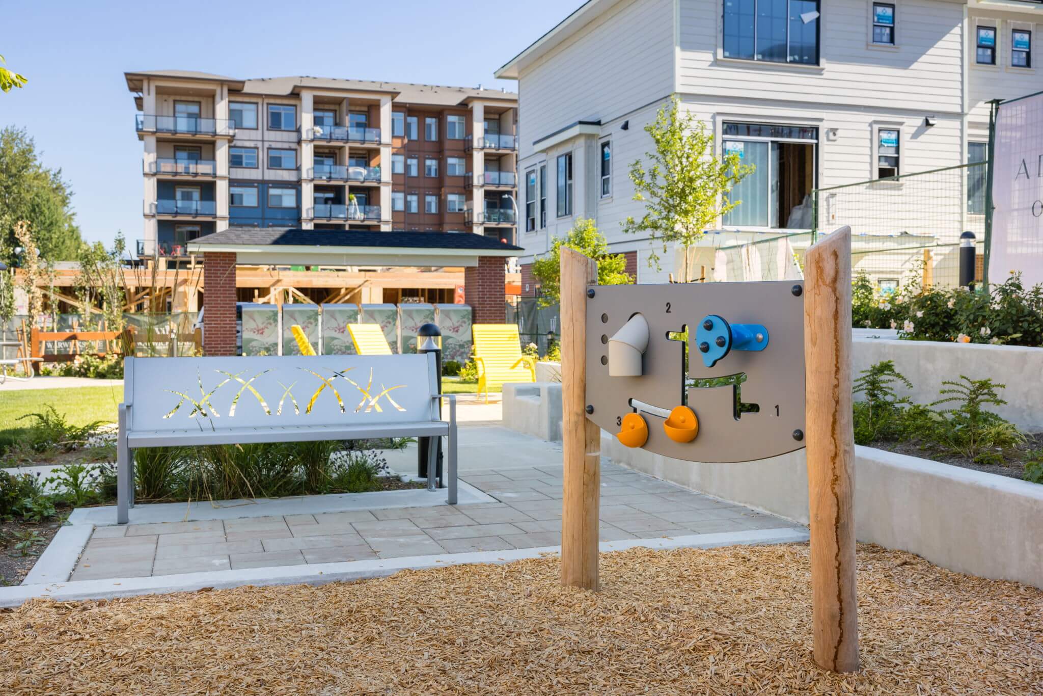 Townside Village – Photo of the community playground with a sensory play panel and bench, condo and townhome buildings in the background.