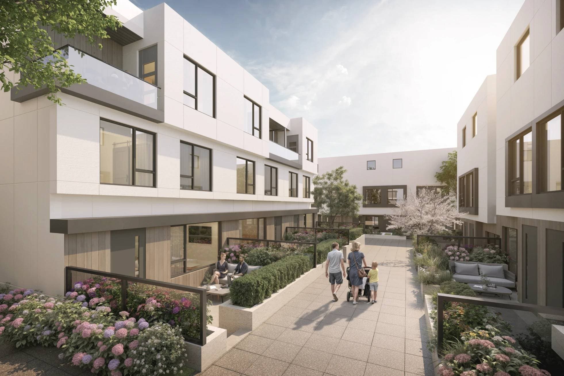 Emera – A family walks along a paved courtyard path between modern white and wood-accented townhomes on a bright, sunny day. Private patio spaces are lined with lush garden beds filled with blooming pink hydrangeas and green shrubbery.
