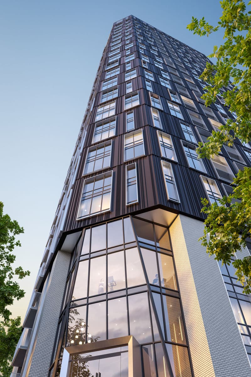 Olo Homes – Upward angled view of the tower's entrance and glass lobby from street level, framed by tree branches.