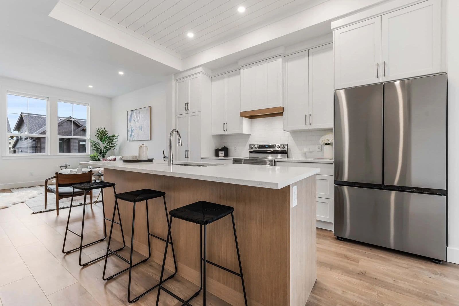 Cedarbrook – A kitchen with white cabinetry, a wood-toned island with black stools, and a stainless steel french-door refrigerator.