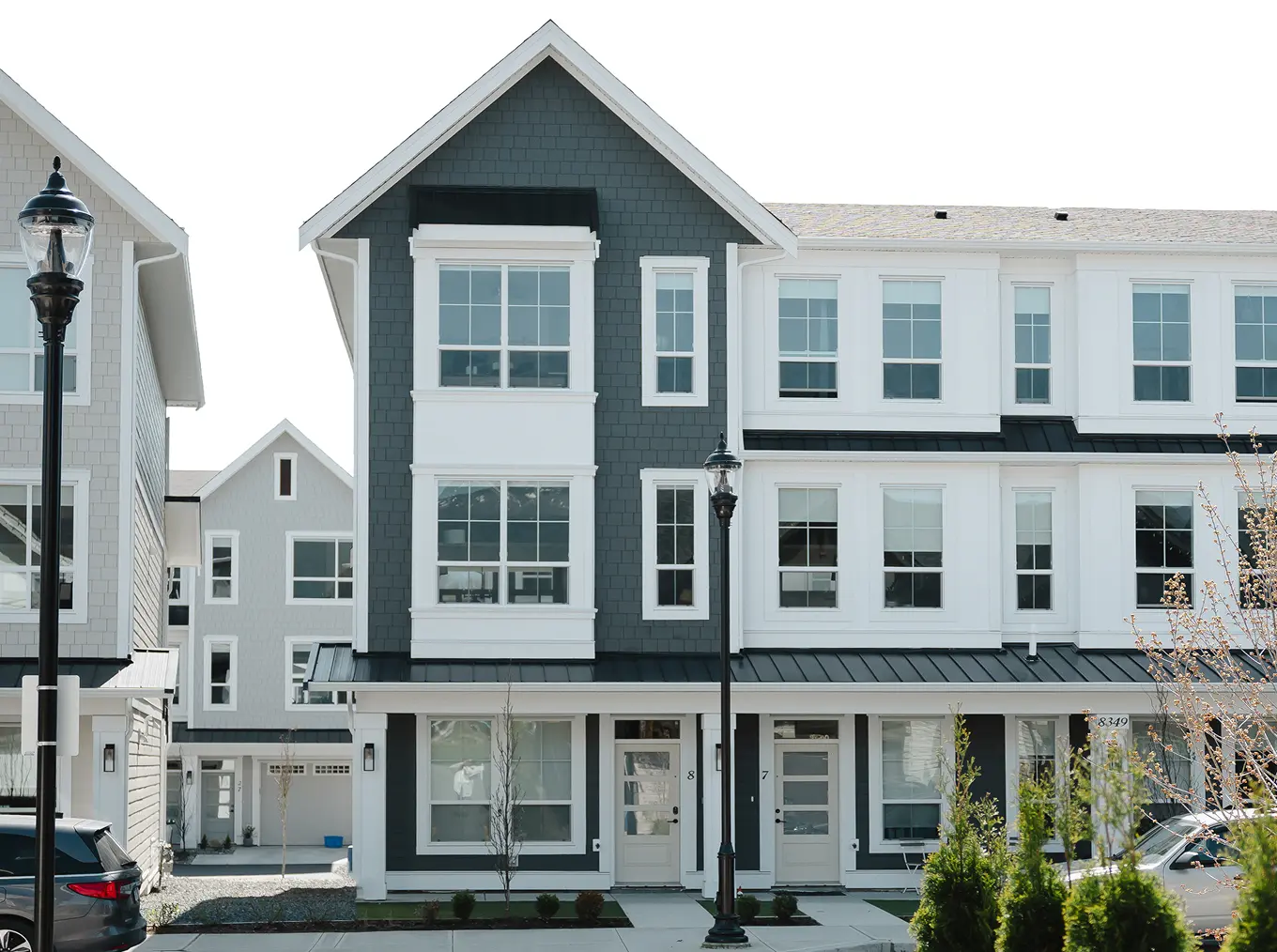 Cedarbrook – Street-level view of a row of three-story townhomes with dark grey shingle siding, white trim, and ground-floor entry doors.