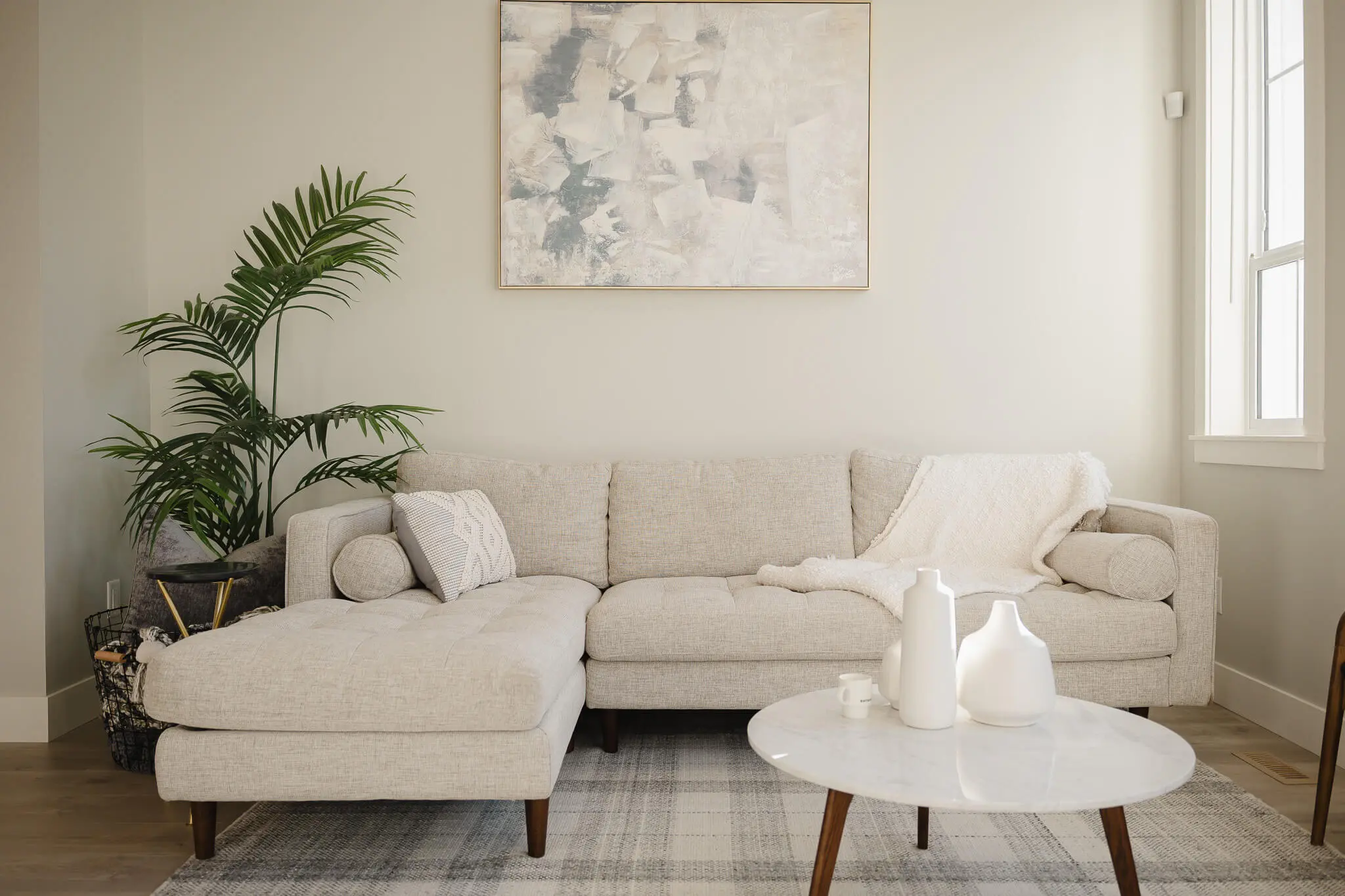 Cedarbrook – A living room with a beige sectional sofa, a potted palm plant, and abstract framed art on the wall above.