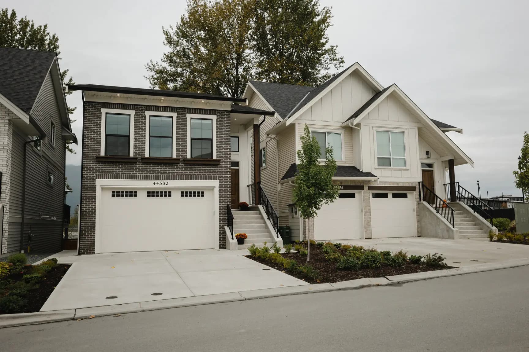 Cedarbrook – Street view of two townhome-style single family homes, one with dark brick and one with light siding, each with double garages.