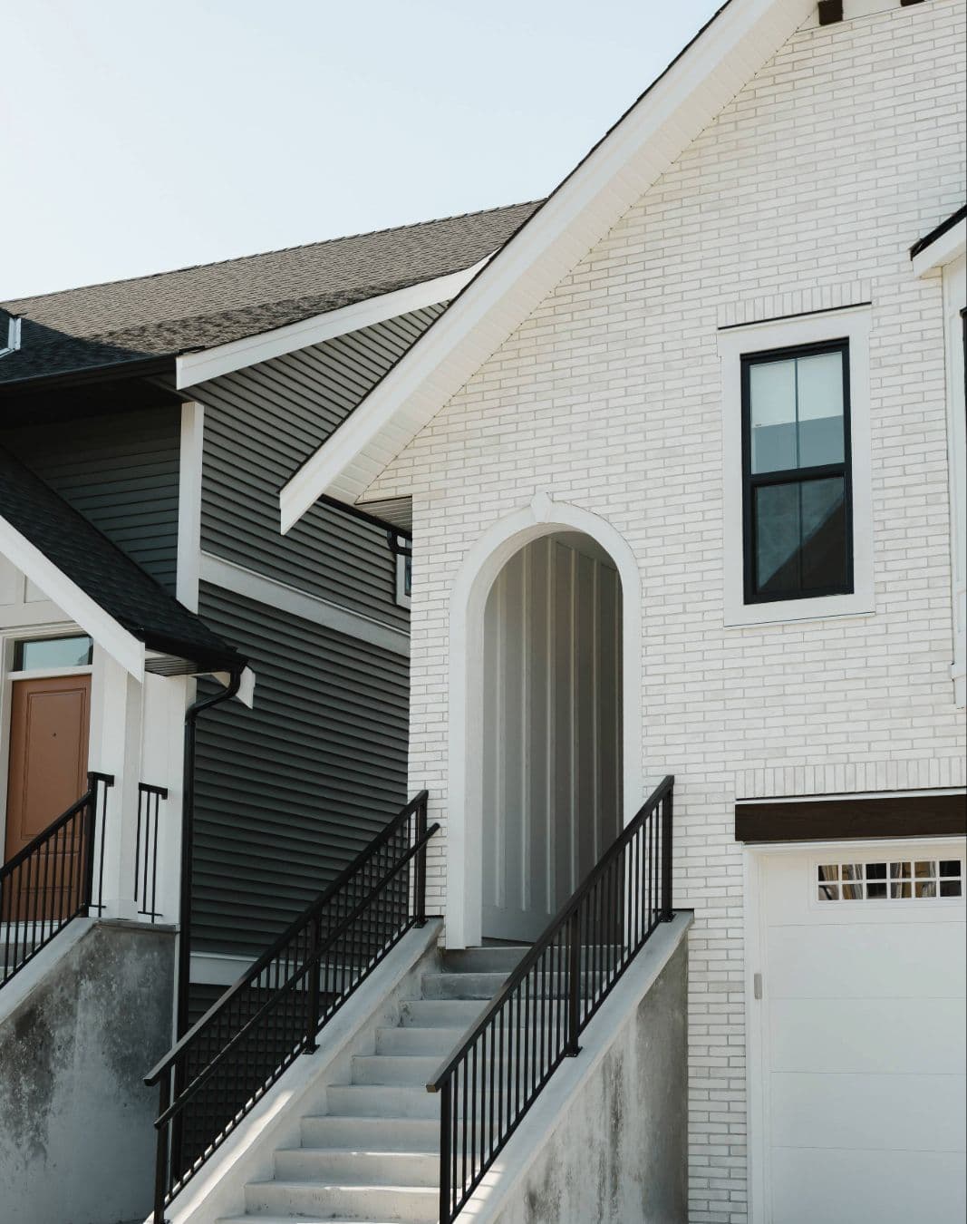 Cedarbrook – Entrance stairway of a white brick home with an arched front door and black metal railings, next to a garage.