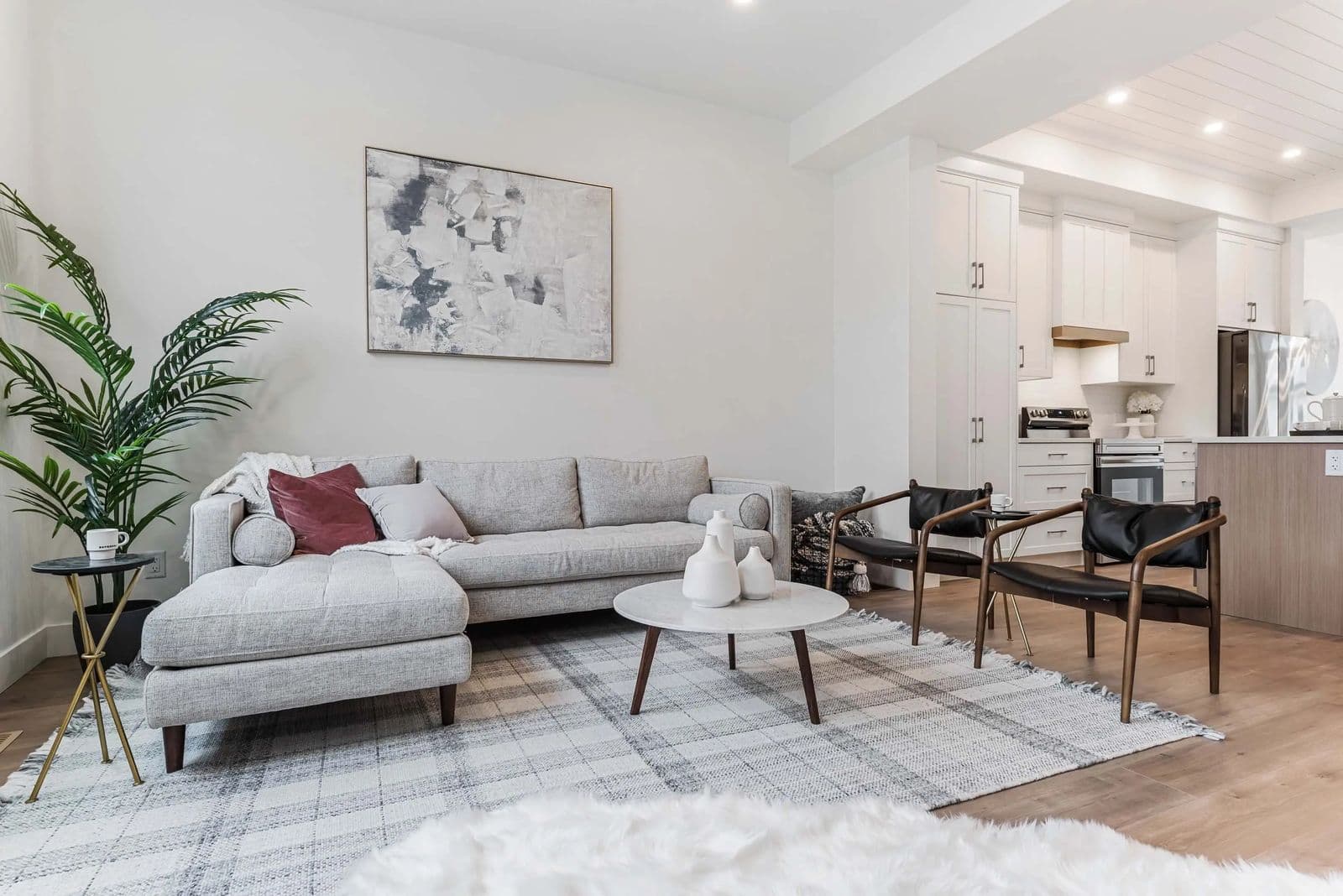Cedarbrook – A living room with a grey sectional sofa, a round marble coffee table, two black leather accent chairs, and an open kitchen in the background.
