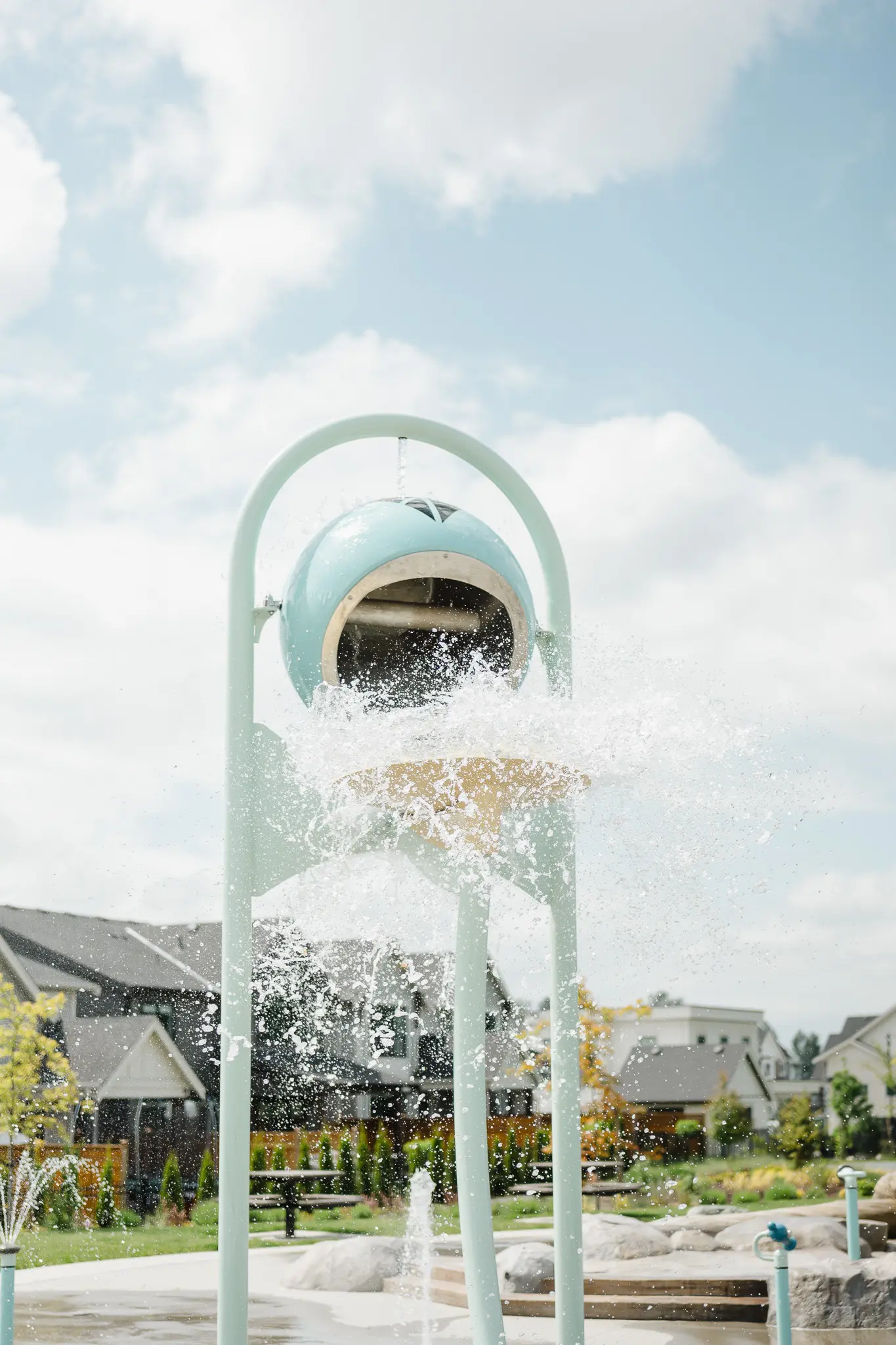 Cedarbrook – A close-up of a splash pad water feature spraying water, with townhomes visible in the background.