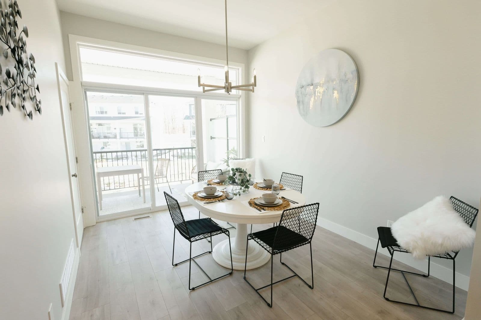 Cedarbrook – A dining nook with a round white pedestal table, black wire chairs, and a sliding glass door leading to a balcony.