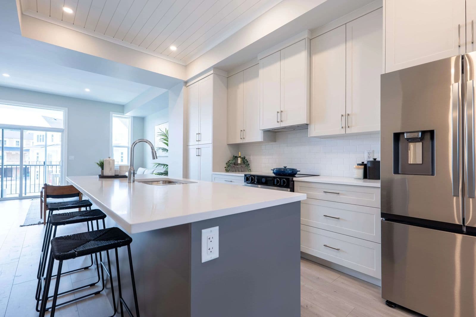 Cedarbrook – A kitchen with white cabinets, a grey-fronted island with white countertop, and a stainless steel fridge with water/ice dispenser.