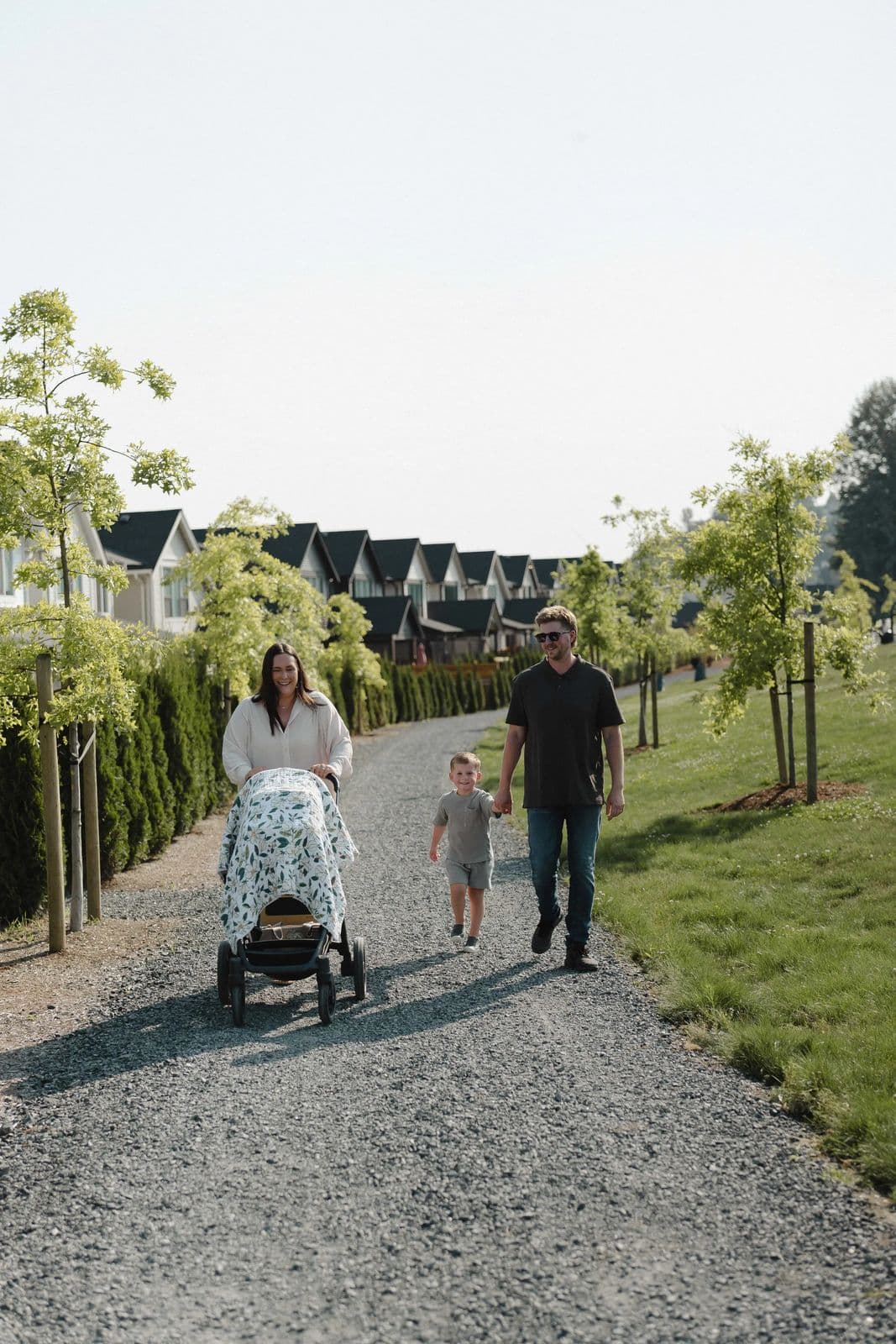 Cedarbrook – A family walks along a gravel path lined with young trees, with a row of townhomes visible in the background.