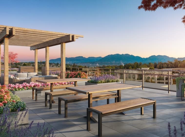 Valeo – Rooftop terrace with a wood pergola, lounge seating, communal picnic tables, and flowering planters overlooking mountains at sunset.