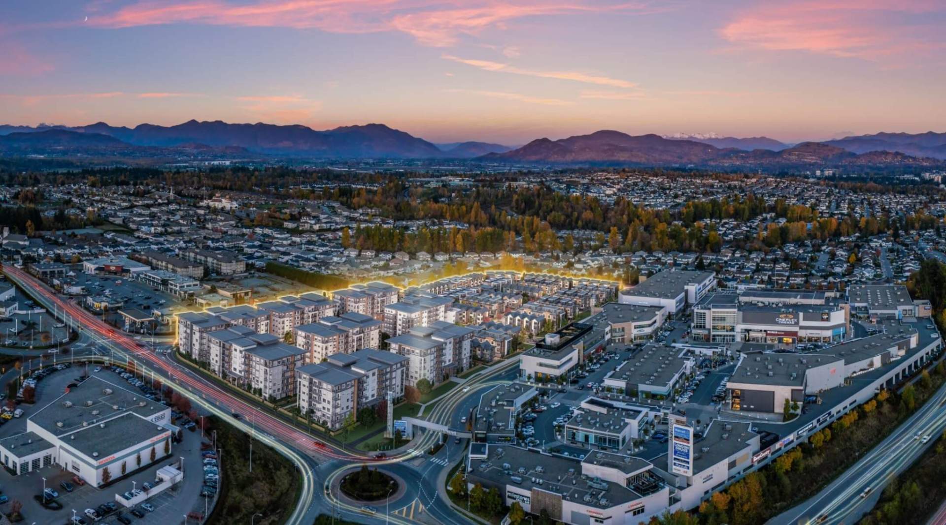 Highstreet Village – Aerial dusk view of the development's low-rise buildings beside a retail plaza with cinema and stores, mountains in the background.