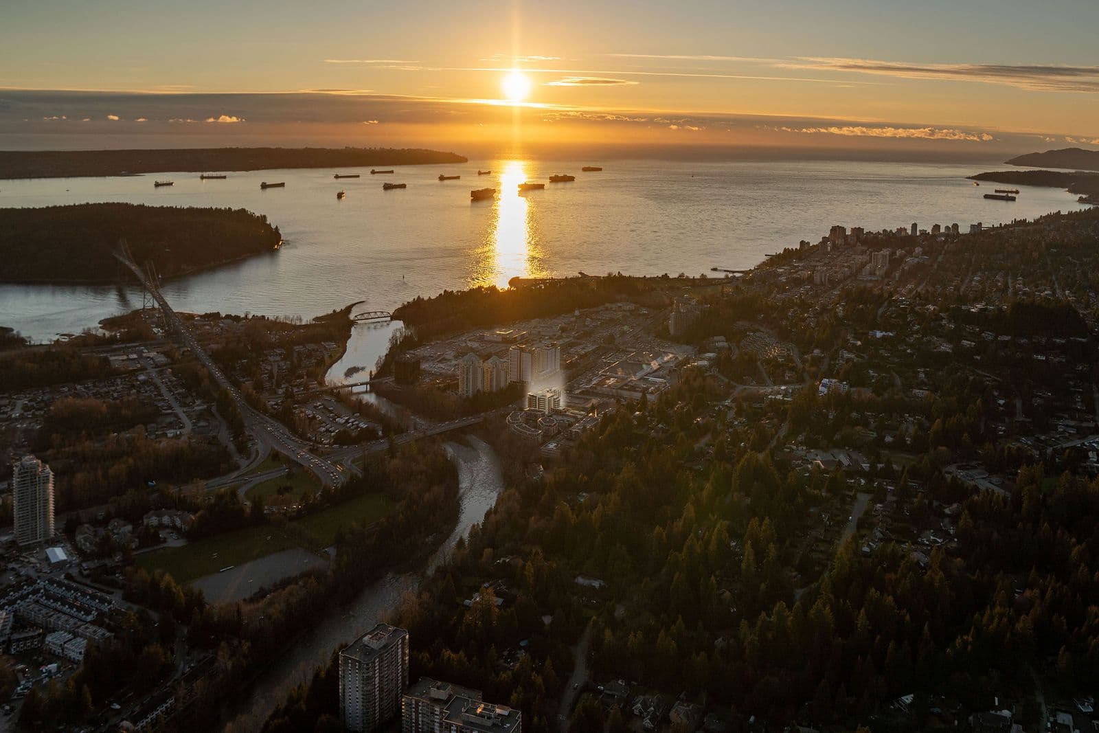 Executive on the Park – Aerial sunset photo over a harbor with cargo ships, a bridge, and the surrounding forested shoreline and city in the distance.