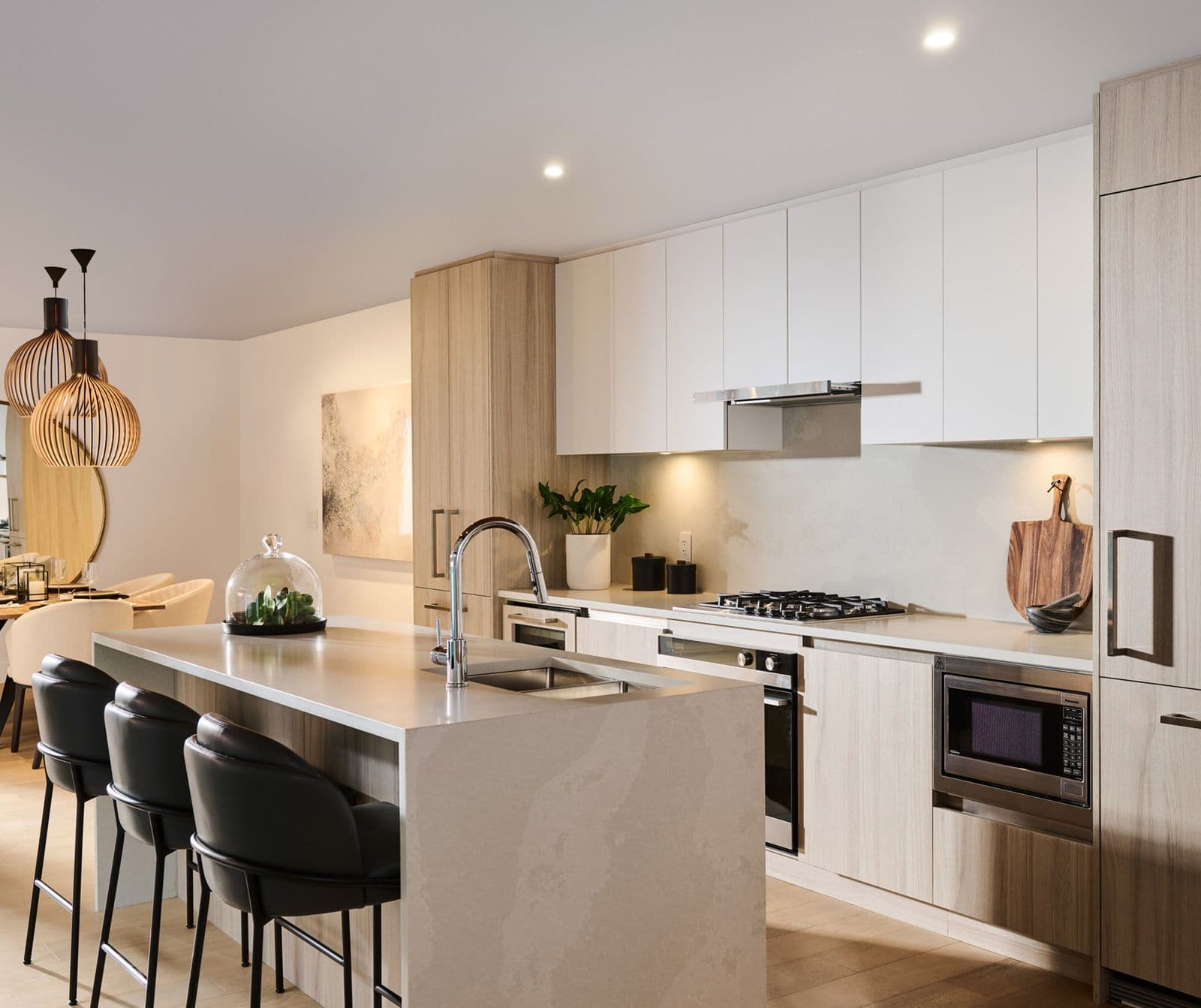 Executive on the Park – Kitchen with white upper cabinets, wood lower cabinets, a gas cooktop, built-in oven, and black bar stools at the island.