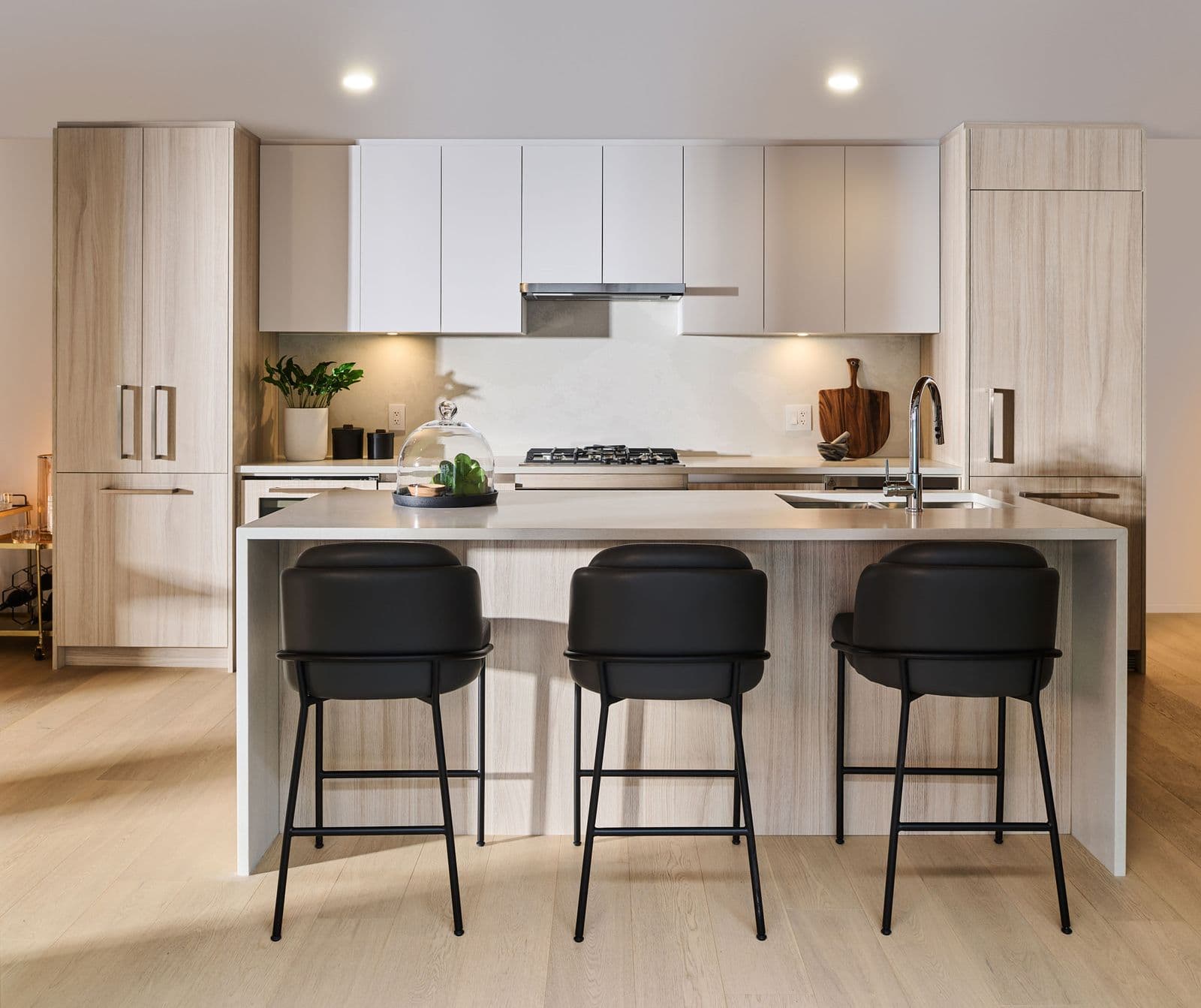 Executive on the Park – Kitchen with light wood and white cabinetry, a large island with black bar stools, and a gas cooktop.