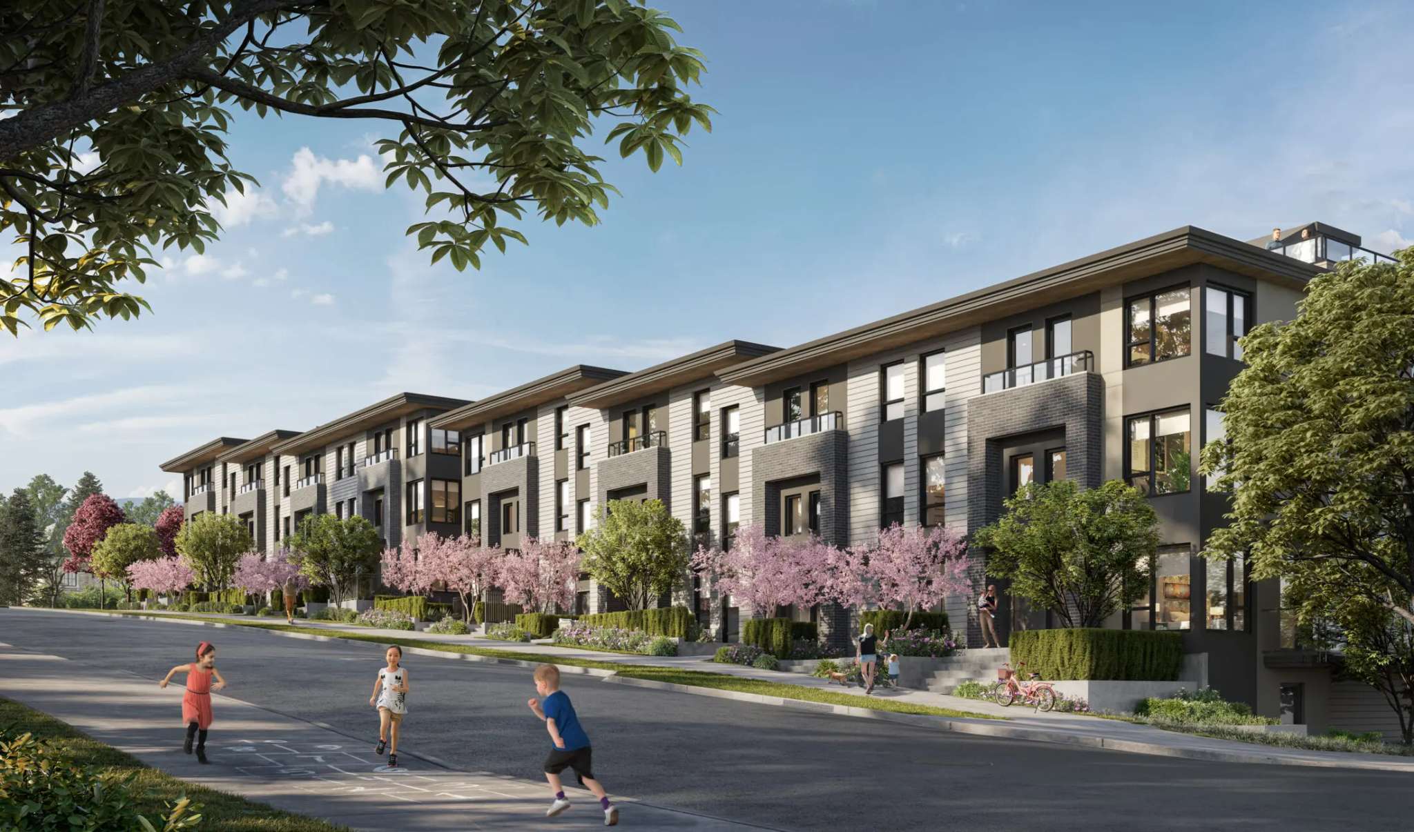 Lodana – A street-level daytime view of a row of townhome-style buildings with grey and beige siding, flowering trees, and children playing on the street.