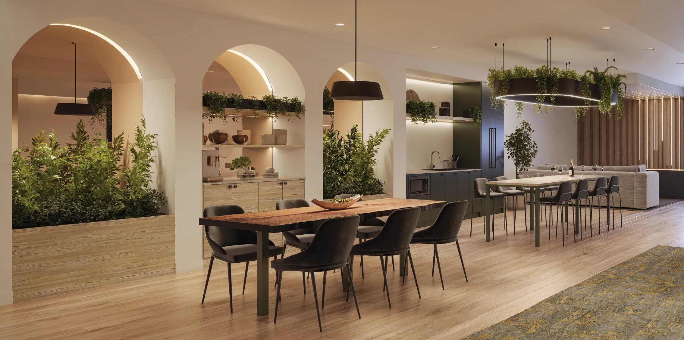Lodana – An arched indoor/lounge corridor with hanging plants, a communal dining table, and a shared kitchenette with bar seating.