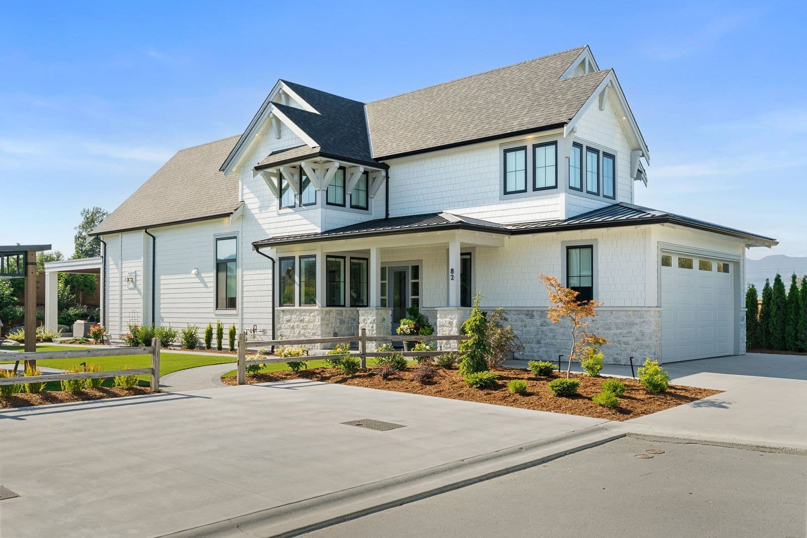 Iron Horse – Two-story white shingle-style house with a covered front porch, stone accents, and a white garage door, address number 82 shown near the entry.