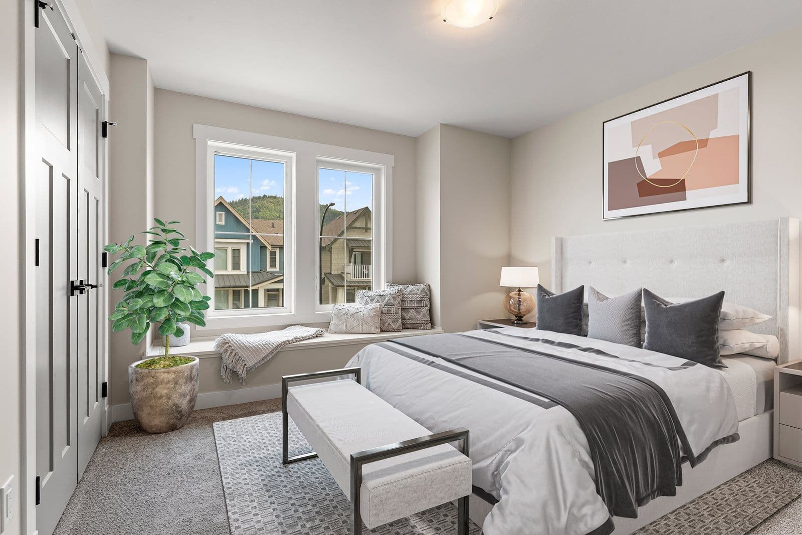 Iron Horse – Bedroom with a king bed with gray and white bedding, a window seat with a throw blanket, a potted plant, and framed abstract art above the headboard.