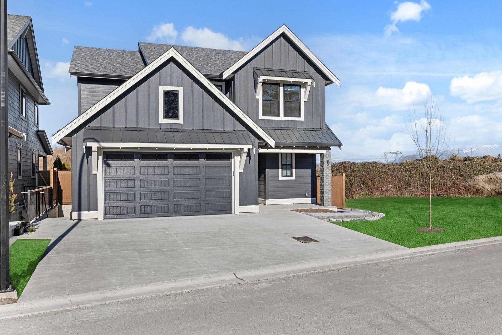 Iron Horse – Two-story gray house with a dark double garage door, front lawn, and a young tree, address number 80 shown on the facade.