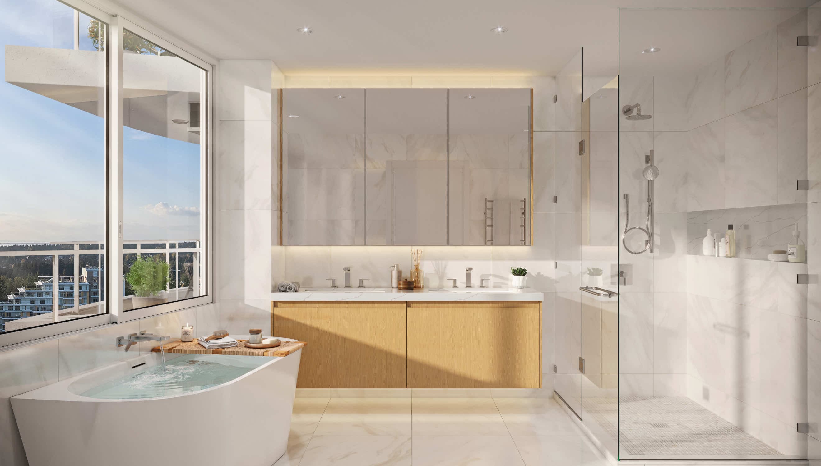Foster Martin – A bright, luxurious bathroom featuring white marble tile, a freestanding soaking tub next to a large window, a glass-enclosed shower, and a floating wood-grain vanity with backlit mirrored cabinets. Sunlight pours through the window, which looks out onto a balcony and views of trees and distant city buildings under a clear blue sky.