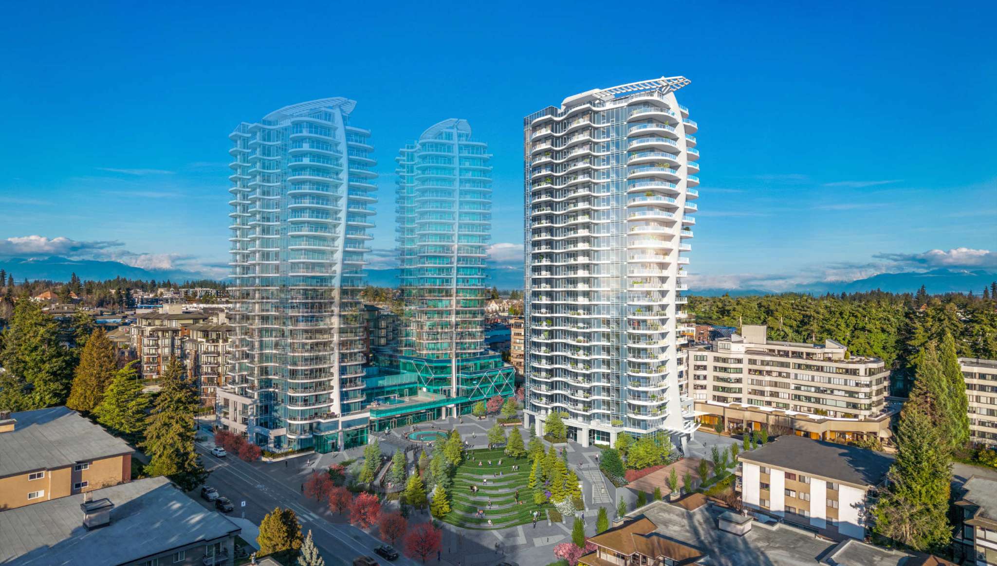 Foster Martin – Elevated aerial view of a multi-tower modern residential complex featuring glass facades, curved white balconies, and a central landscaped public plaza with amphitheater-style stepped lawns. The surrounding neighborhood is filled with lush green trees and low-rise buildings beneath a bright blue sky with distant mountain views.