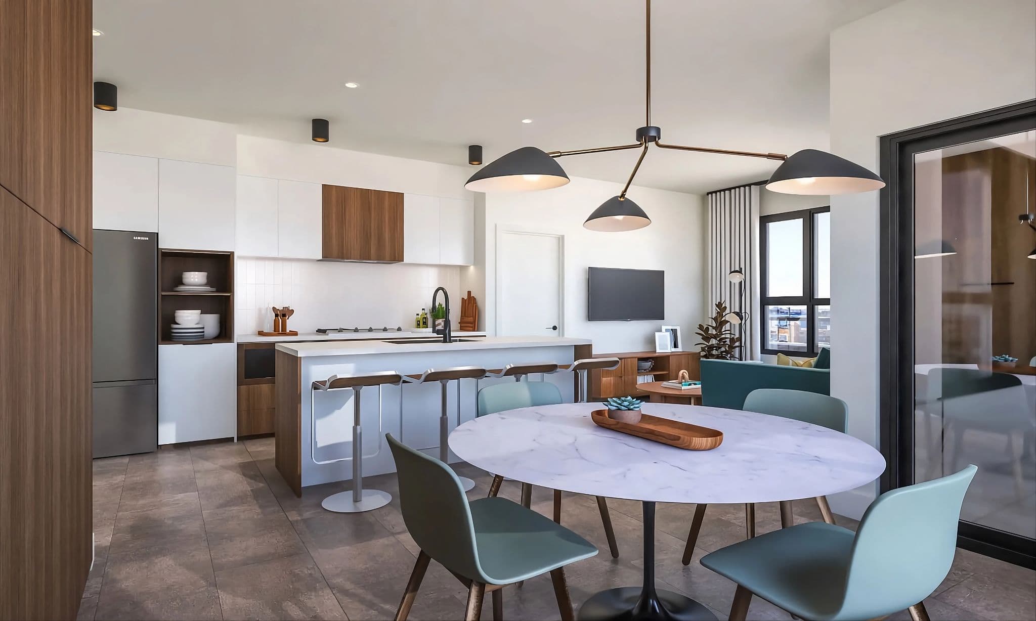 Aavand – A bright, open-concept kitchen and living area featuring a round marble-topped dining table with sage green chairs beneath a modern branched chandelier. The space flows into a contemporary kitchen with white and natural wood cabinetry, a waterfall island with barstools, and an adjacent living room bathed in natural light.