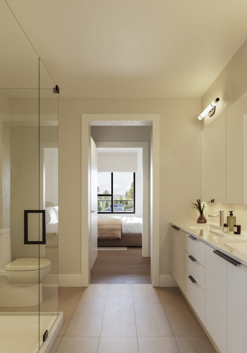 Scott + 77 – A modern ensuite bathroom with a sleek double-sink vanity, glass-enclosed shower, and neutral tile flooring. An open doorway looks directly into an adjoining, bright bedroom featuring a large window with a view of evergreen trees.