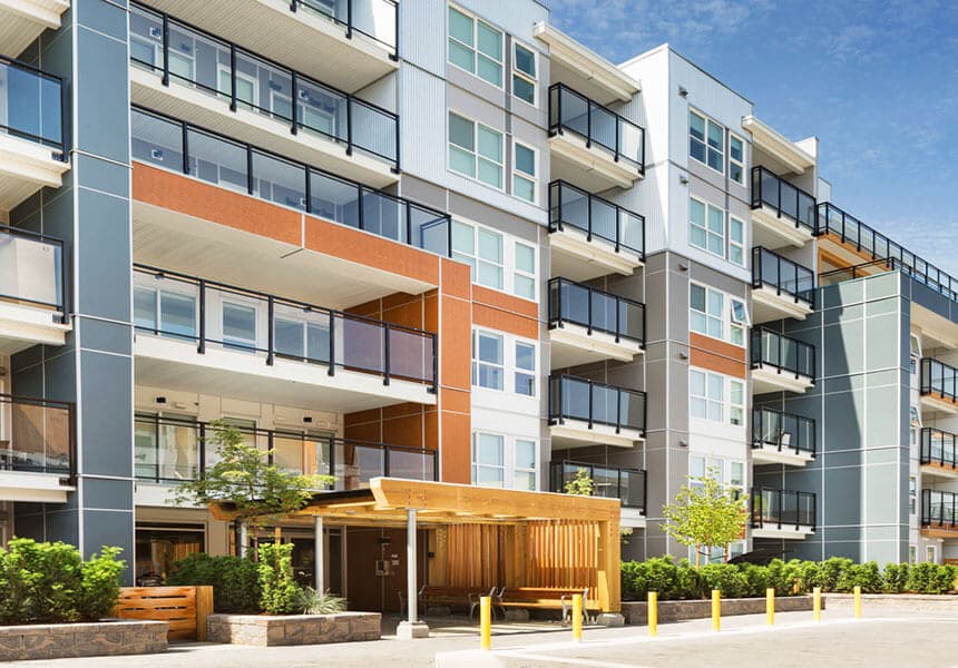 Crescentview at Edgemont – Street-level view of a multi-story condo building with orange and grey siding, private balconies, and a wood-covered entry walkway.