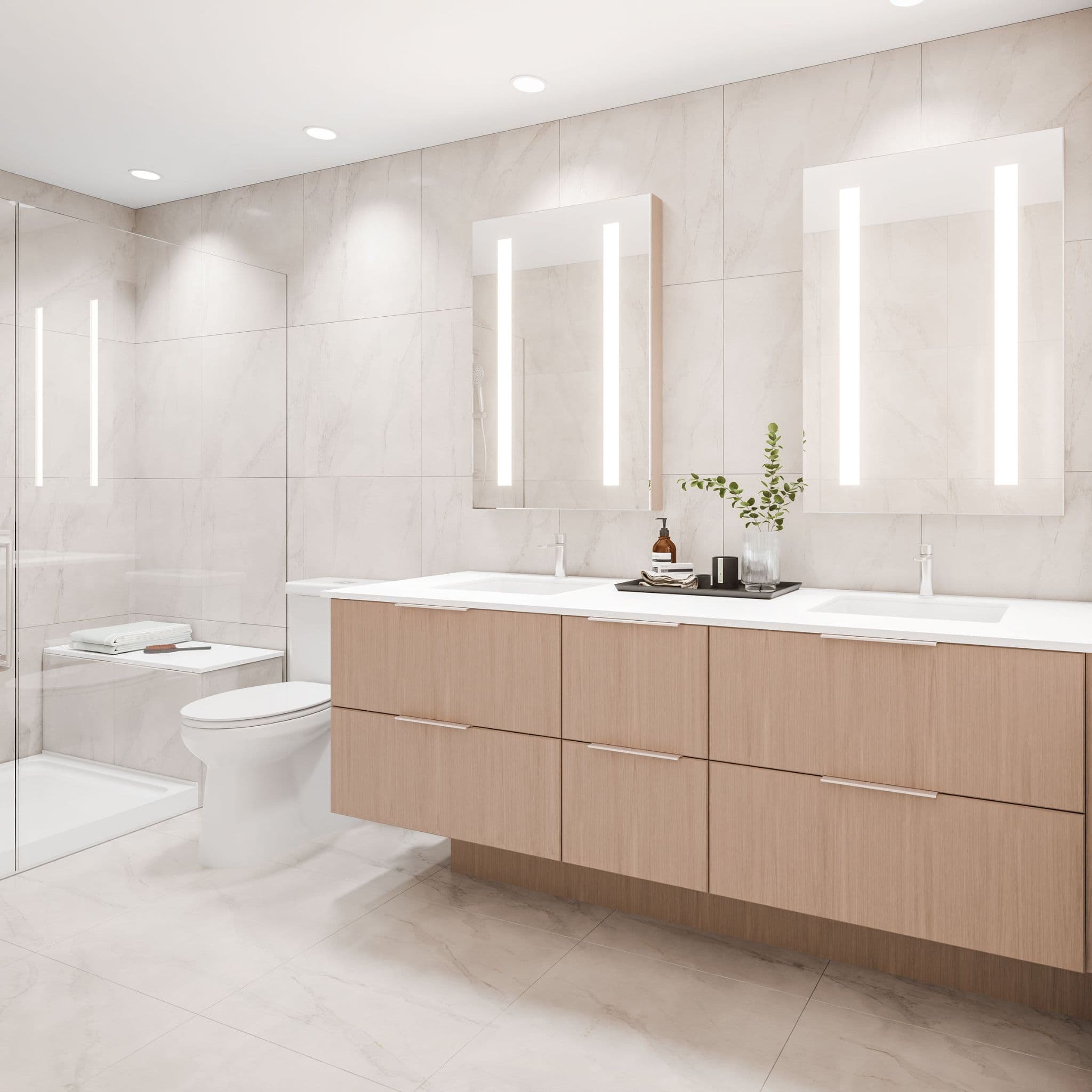 Exeter Hall – A modern, bright bathroom featuring a light wood double vanity with white countertops and two illuminated vertical strip mirrors. The space is fully lined in warm beige marble-look tiles, complete with a glass-enclosed walk-in shower with a built-in bench and a toilet.