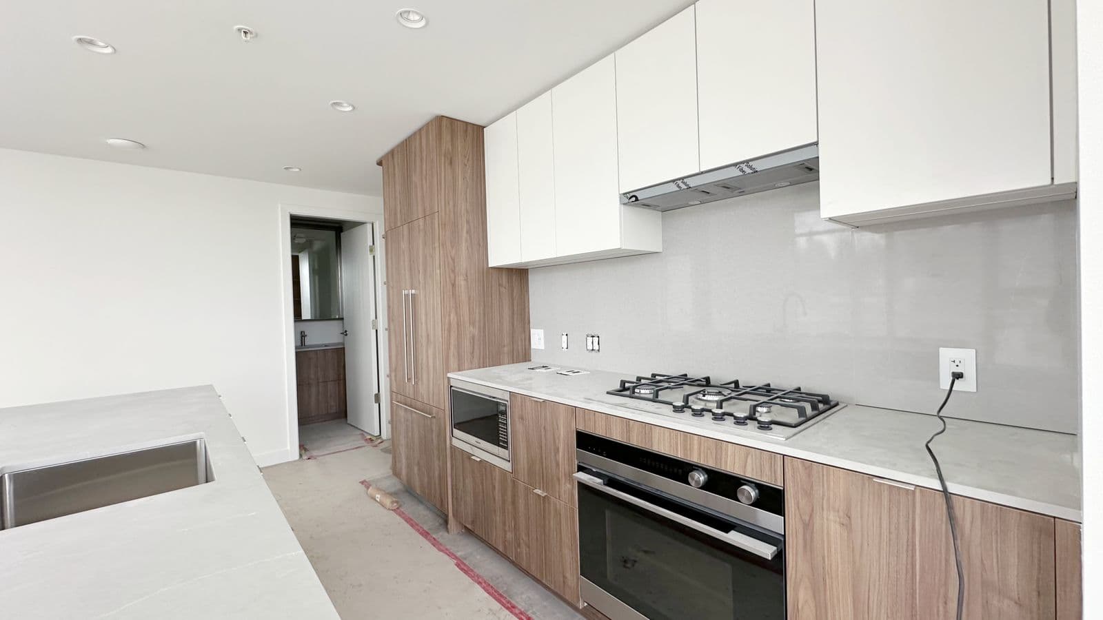 West – Kitchen under construction with white upper cabinets, wood lower cabinets, a gas cooktop, built-in microwave and oven, and protective paper on the countertops and floor.