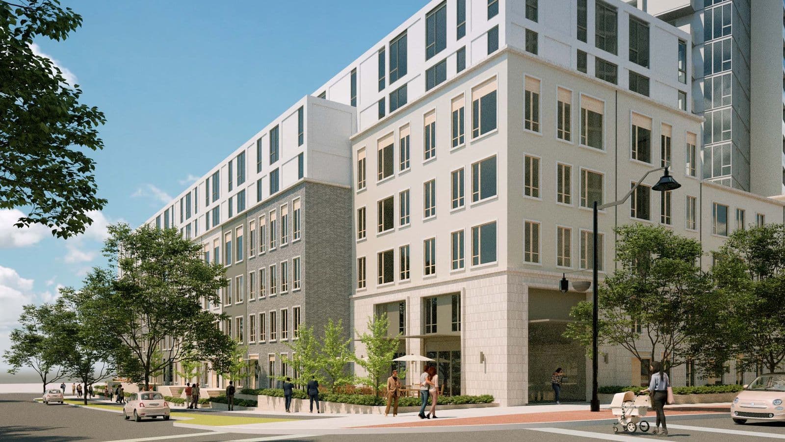 Mackin Parkside – A daytime street-level view of a light-toned mid-rise apartment building with a brick base, ground-floor parking entrance, and people walking past.