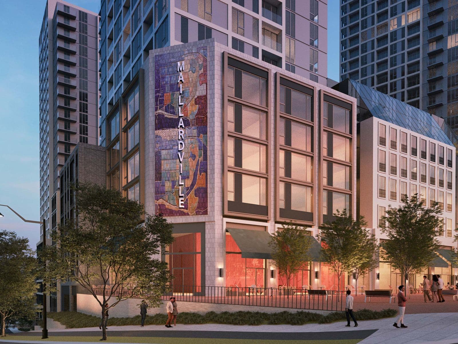 Mackin Parkside – A dusk street view of a tower entrance featuring a large vertical mosaic mural reading 'Maillardville' above ground-floor retail with awnings.
