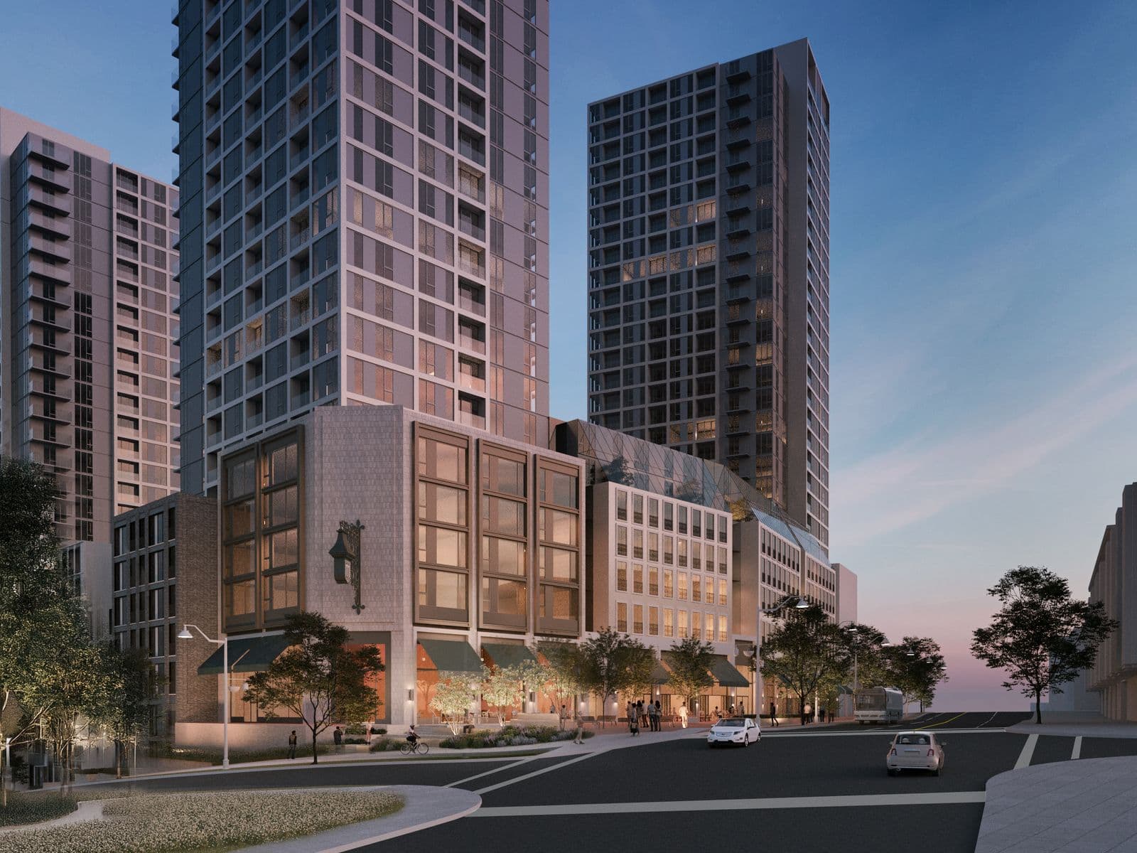 Mackin Parkside – A dusk street-level view of two tall residential towers rising above a mid-rise retail podium with awnings and outdoor cafe seating.