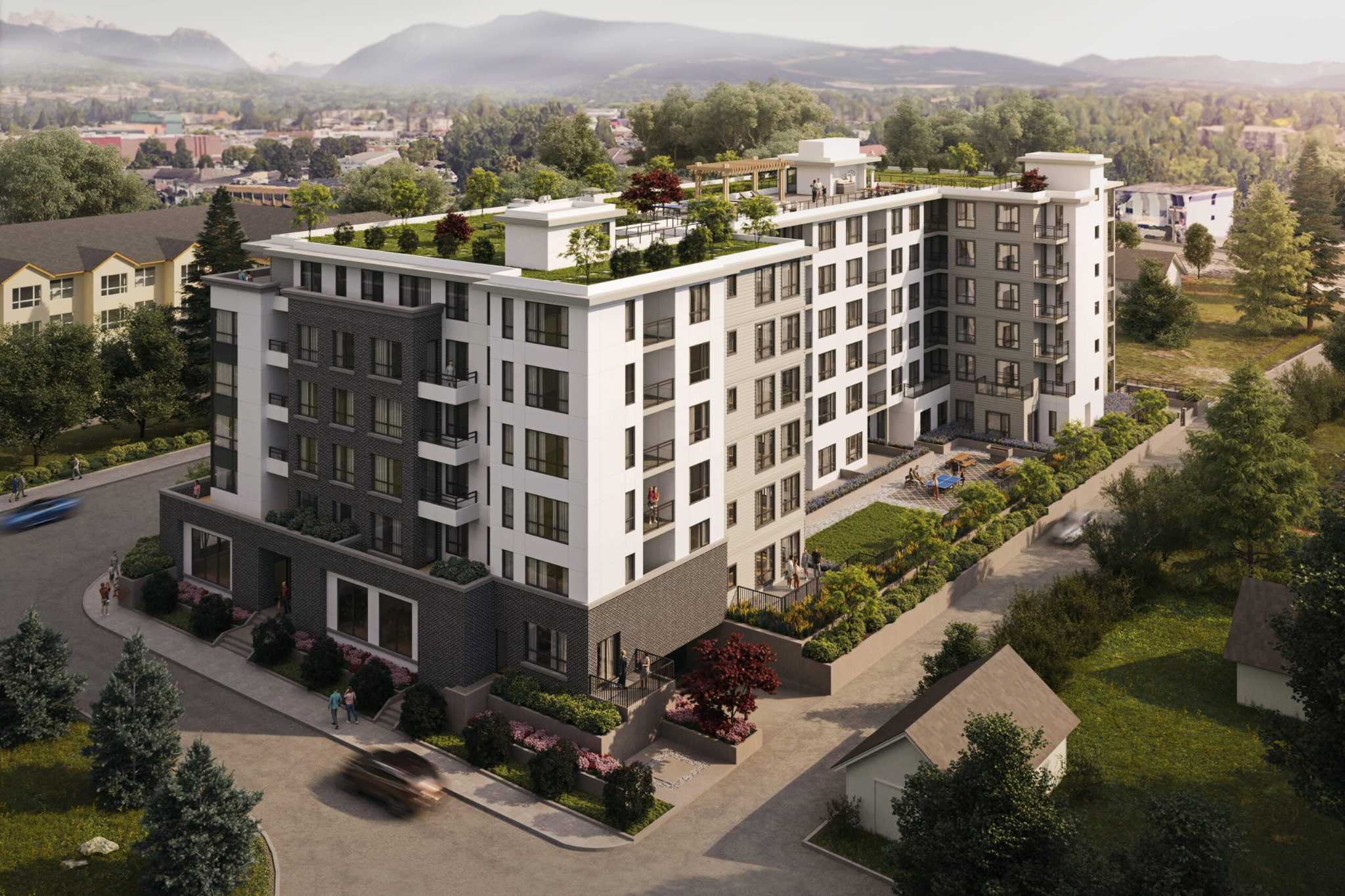 La Riviere – An aerial daytime view of a mid-rise apartment building with a rooftop garden terrace, set against mountains in the background.