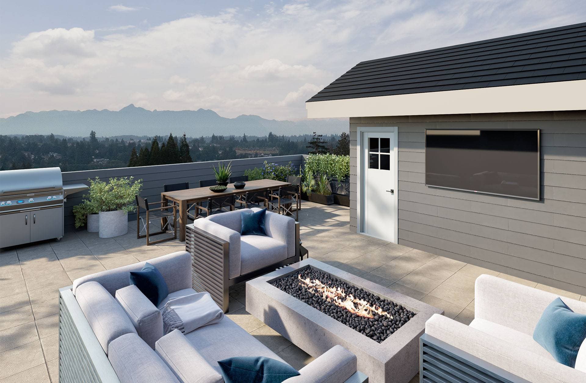 Harmony – A paved outdoor rooftop terrace features a concrete fire pit surrounded by cushioned lounge seating, an outdoor dining table, a stainless steel BBQ grill, and an exterior wall-mounted TV. The space overlooks lush green treetops and distant mountain ranges under a clear, bright daytime sky.