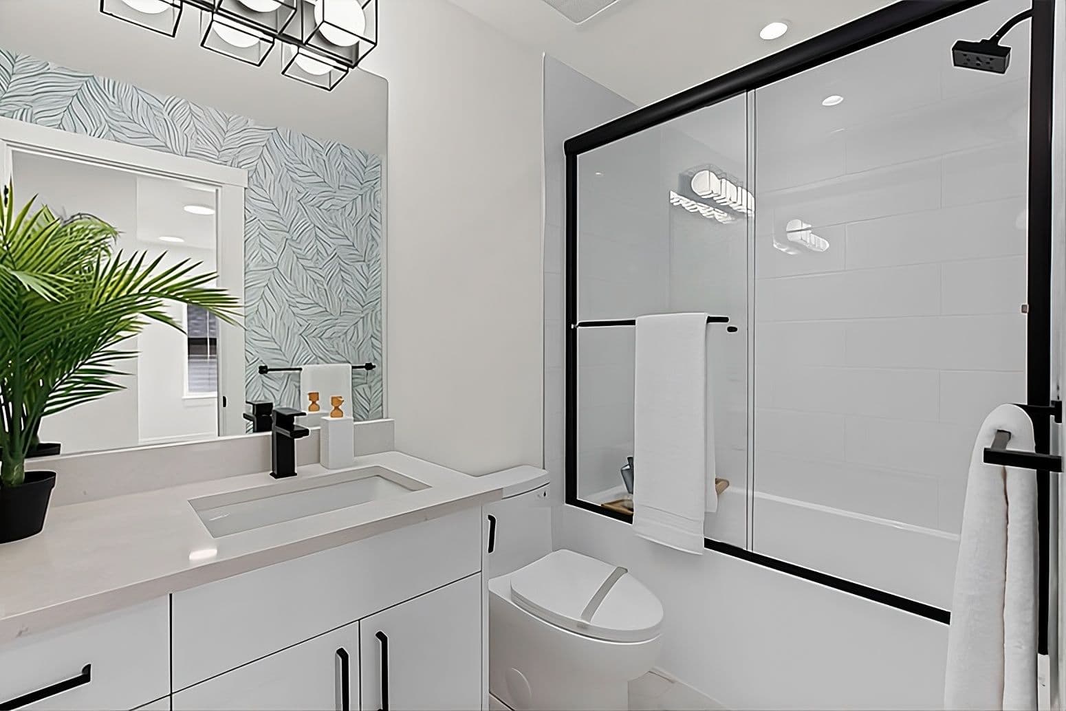 Harmony – Bathroom with tropical leaf-patterned wallpaper, black fixtures, a potted plant, and a glass-and-tile shower/tub combo.